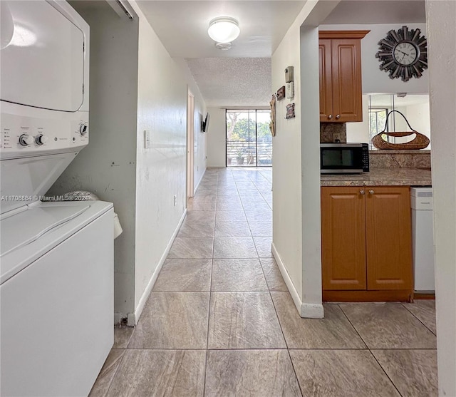 laundry room featuring light tile patterned floors, a textured ceiling, and stacked washer and clothes dryer