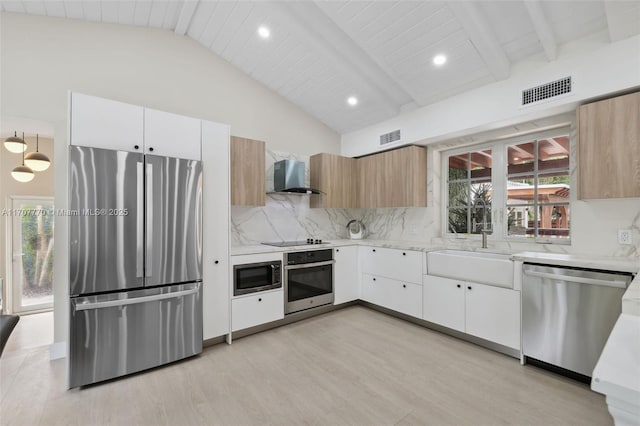 kitchen featuring lofted ceiling with beams, white cabinetry, backsplash, stainless steel appliances, and wall chimney exhaust hood