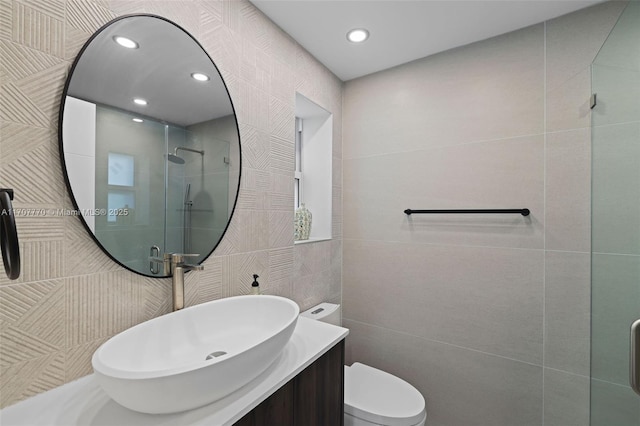 bathroom with vanity, toilet, a shower with door, and tile walls