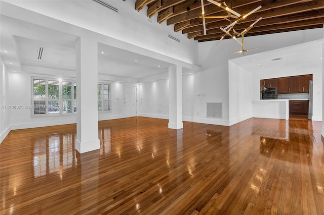 unfurnished living room with hardwood / wood-style floors, beamed ceiling, and high vaulted ceiling