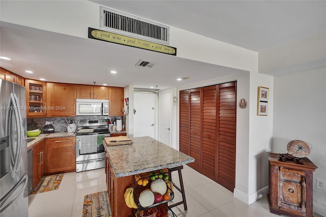 kitchen featuring appliances with stainless steel finishes, backsplash, light stone counters, a kitchen island, and light tile patterned flooring