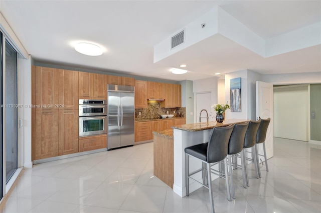 kitchen with light stone countertops, decorative backsplash, a kitchen bar, stainless steel appliances, and sink