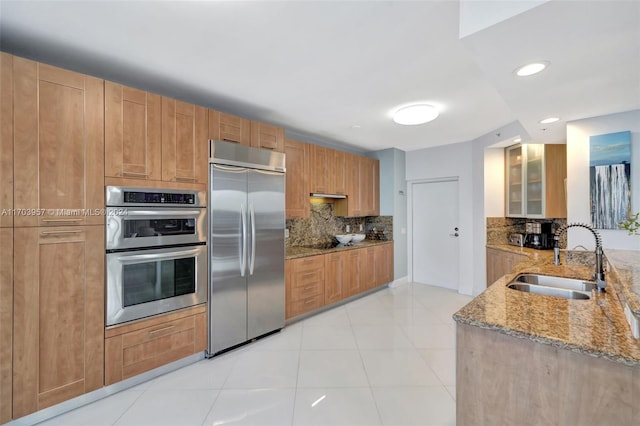 kitchen featuring sink, tasteful backsplash, light stone counters, light tile patterned floors, and appliances with stainless steel finishes