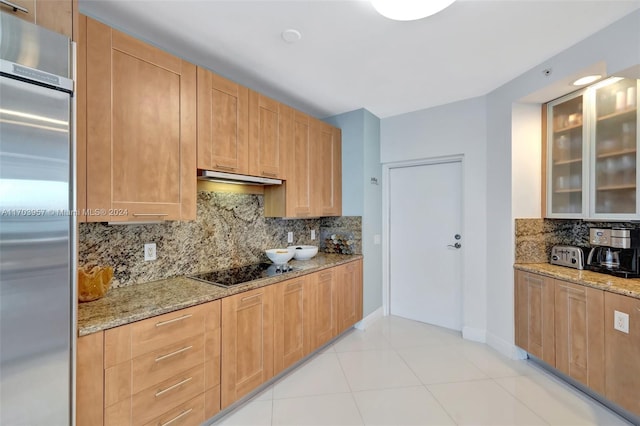 kitchen featuring decorative backsplash, black electric cooktop, light stone counters, and built in fridge