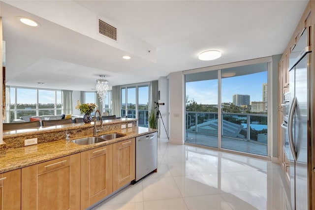 kitchen featuring sink, light tile patterned floors, appliances with stainless steel finishes, a notable chandelier, and light stone counters