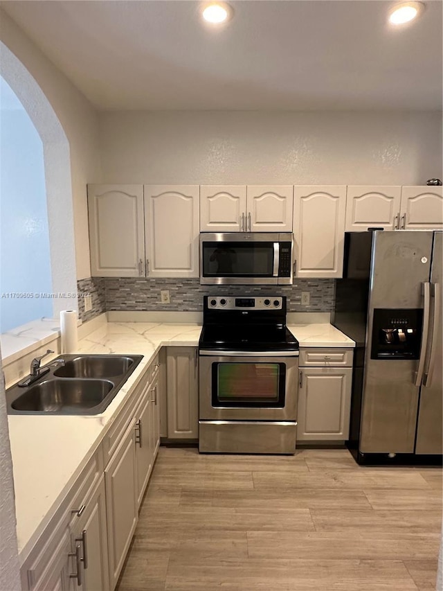 kitchen with decorative backsplash, stainless steel appliances, sink, light hardwood / wood-style flooring, and white cabinets