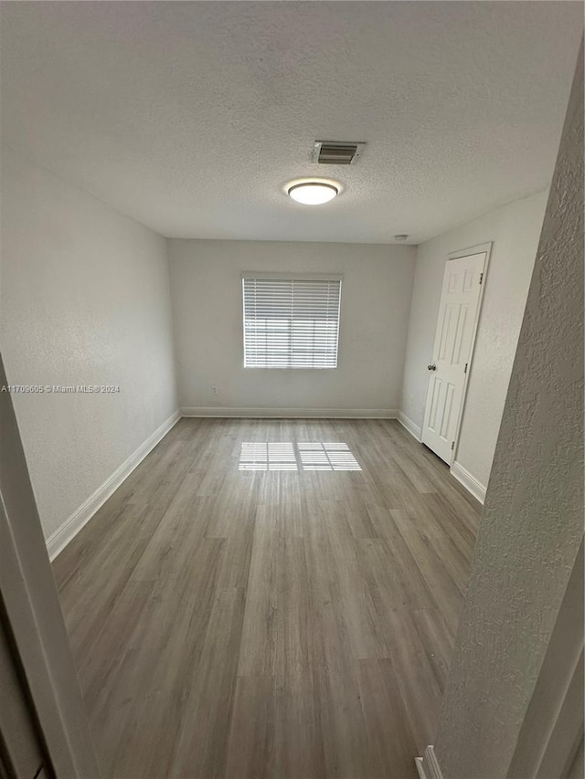 empty room with light wood-type flooring and a textured ceiling