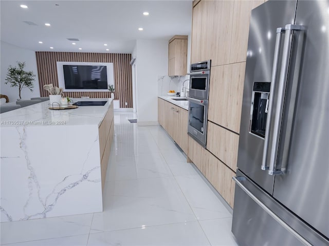 kitchen with sink, light stone counters, light brown cabinetry, a kitchen island, and appliances with stainless steel finishes