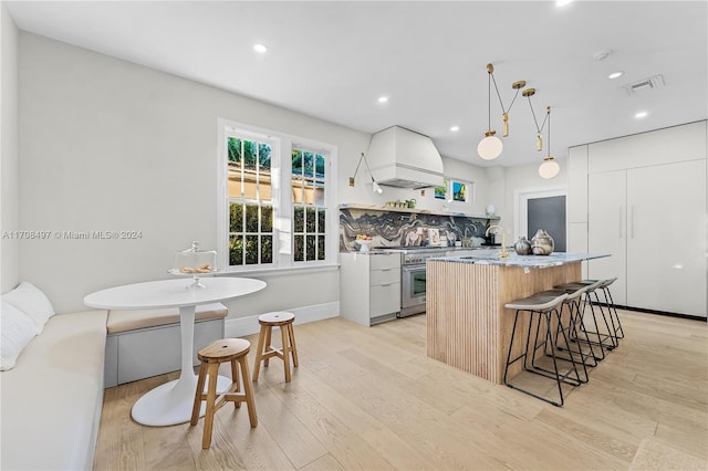 kitchen with white cabinetry, light hardwood / wood-style flooring, high end stove, decorative light fixtures, and custom exhaust hood