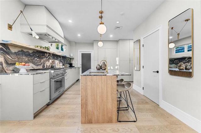 kitchen featuring custom exhaust hood, white cabinets, hanging light fixtures, stainless steel stove, and a kitchen island