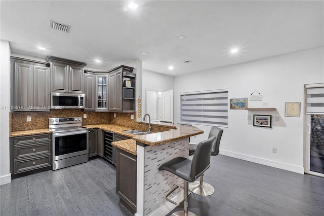 kitchen with light stone countertops, sink, stainless steel appliances, dark hardwood / wood-style floors, and kitchen peninsula