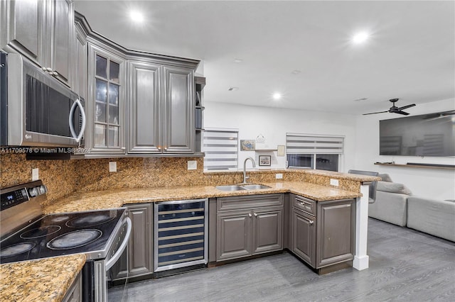 kitchen with light stone countertops, sink, wine cooler, appliances with stainless steel finishes, and hardwood / wood-style flooring