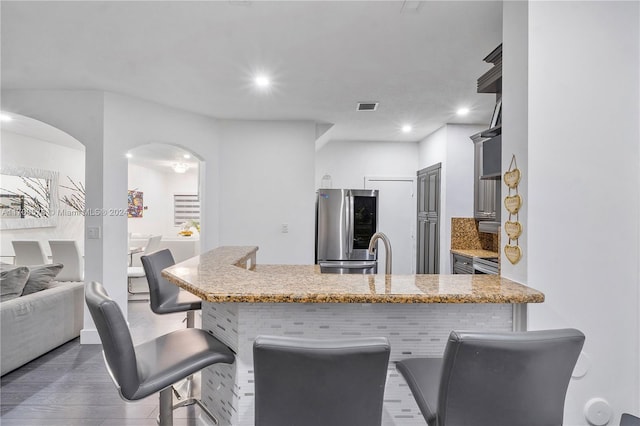 kitchen featuring stainless steel refrigerator, light stone countertops, sink, dark wood-type flooring, and kitchen peninsula