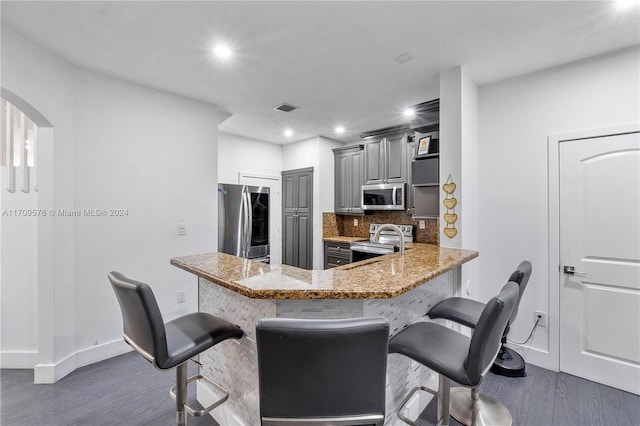 kitchen with gray cabinetry, a kitchen breakfast bar, kitchen peninsula, and appliances with stainless steel finishes