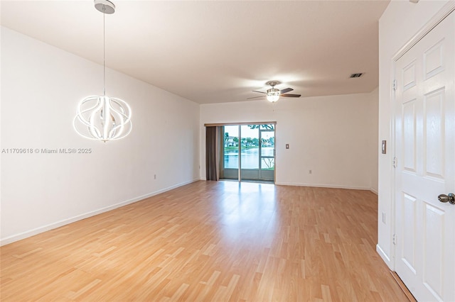 spare room featuring visible vents, light wood-style flooring, ceiling fan with notable chandelier, and baseboards