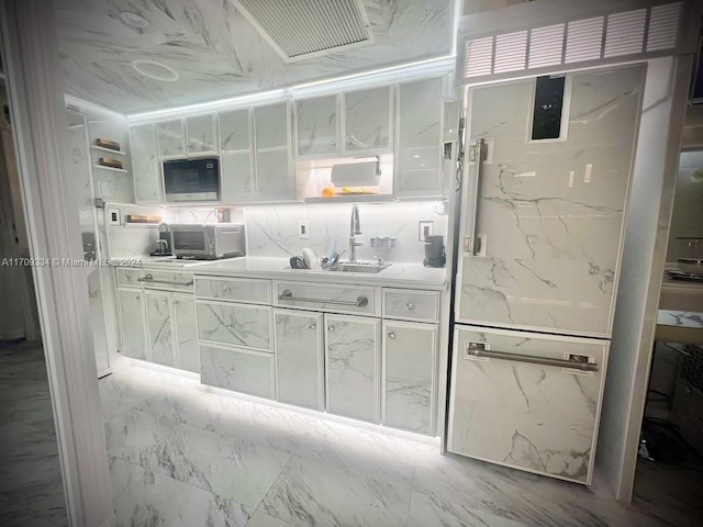 kitchen featuring white cabinets, decorative backsplash, stainless steel microwave, and sink