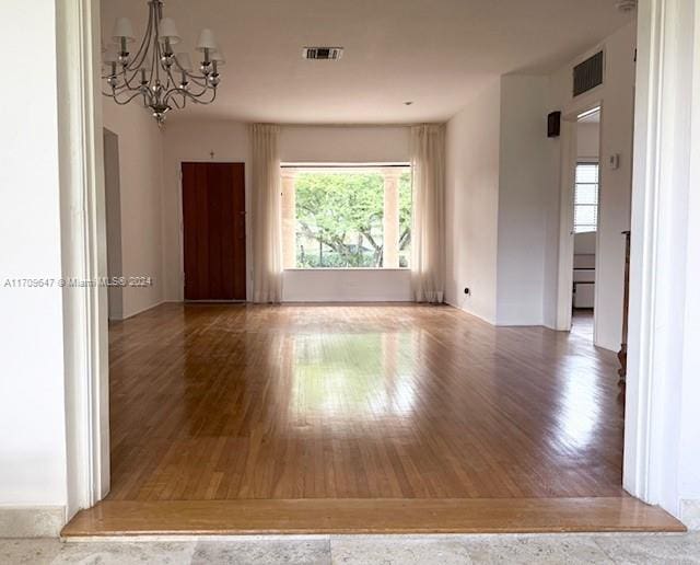 empty room with hardwood / wood-style floors and an inviting chandelier