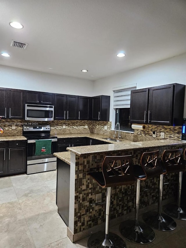 kitchen featuring sink, light stone counters, kitchen peninsula, a kitchen bar, and appliances with stainless steel finishes