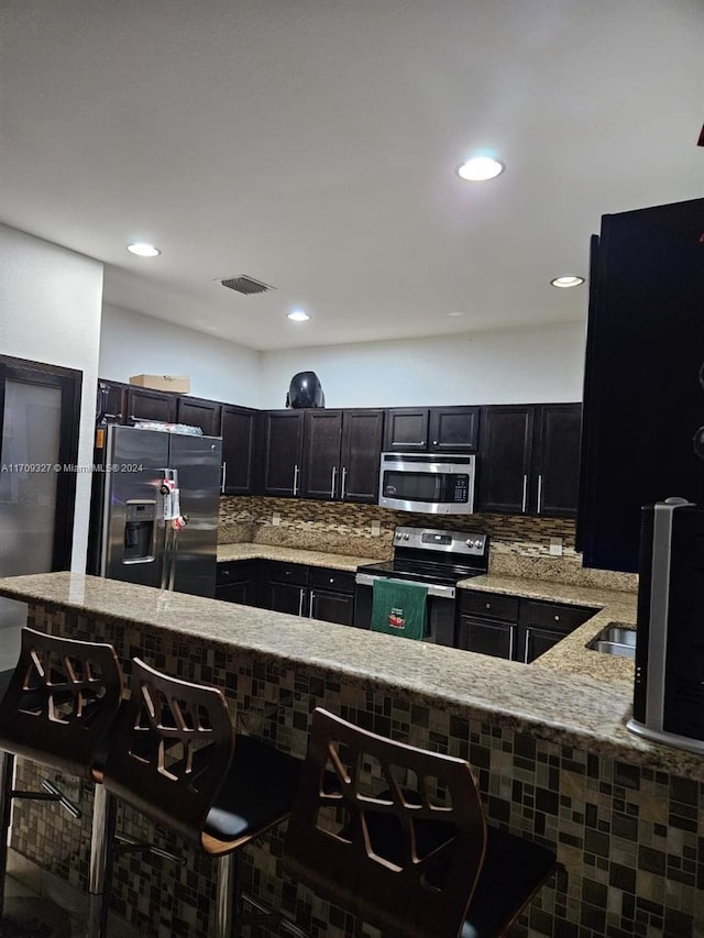 kitchen with stainless steel appliances, light stone counters, kitchen peninsula, a kitchen bar, and decorative backsplash