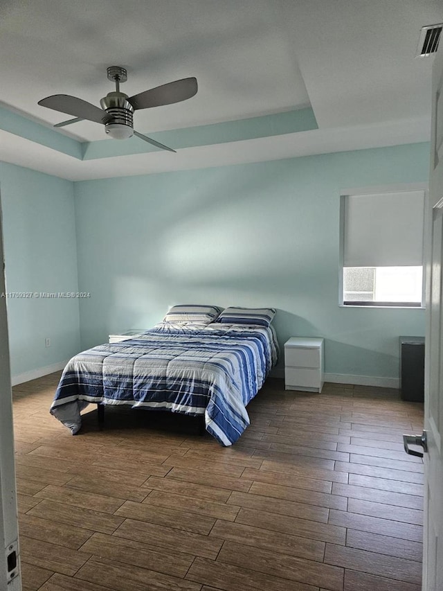 bedroom with ceiling fan, dark wood-type flooring, and a tray ceiling