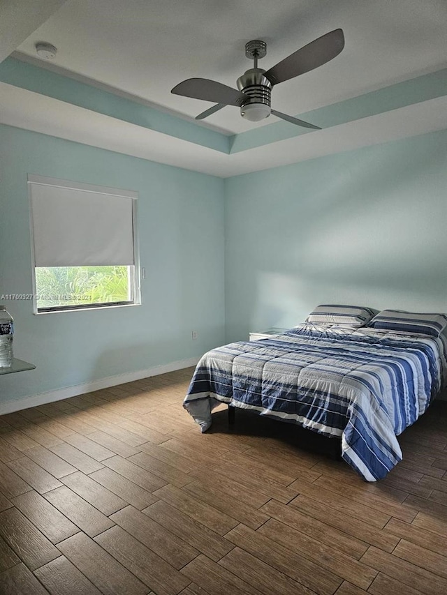 bedroom with a raised ceiling, ceiling fan, and dark wood-type flooring