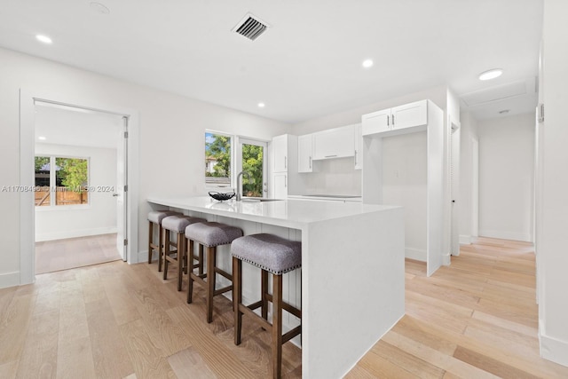 kitchen with a breakfast bar area, sink, white cabinets, and light hardwood / wood-style floors