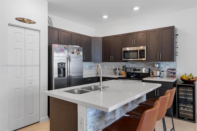 kitchen featuring a center island with sink, sink, a kitchen bar, stainless steel appliances, and beverage cooler