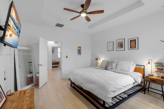 bedroom with a raised ceiling, ceiling fan, and light hardwood / wood-style flooring