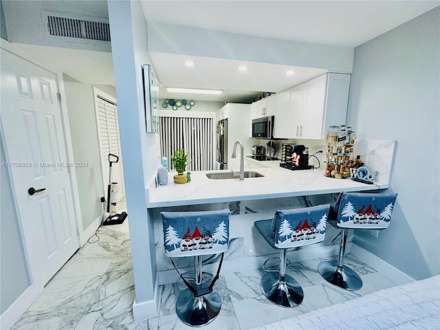 kitchen featuring kitchen peninsula, a kitchen breakfast bar, stainless steel appliances, sink, and white cabinetry