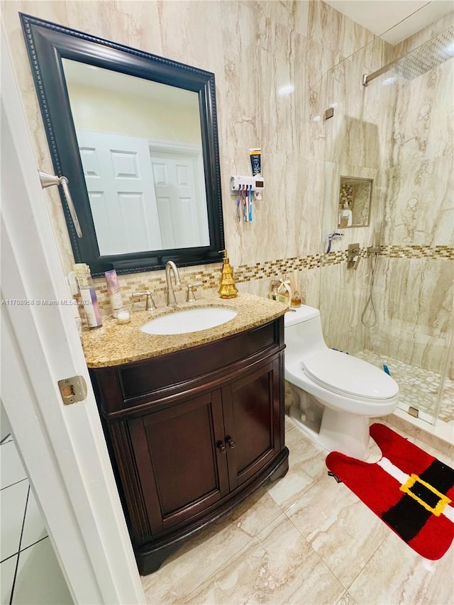 bathroom with tiled shower, vanity, toilet, and tile walls