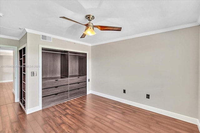 unfurnished bedroom with crown molding, wood-type flooring, a closet, and ceiling fan