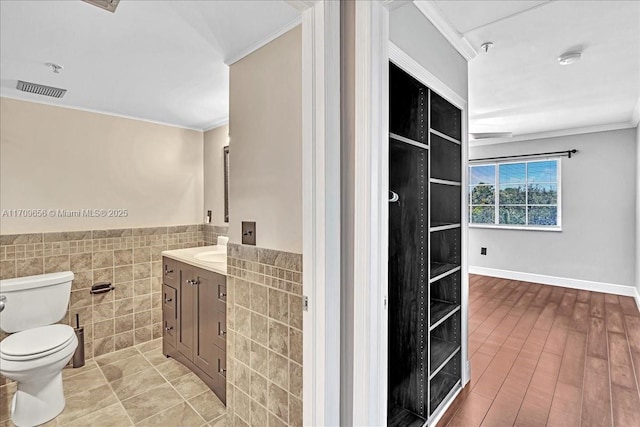 bathroom with tile walls, hardwood / wood-style floors, vanity, ornamental molding, and toilet