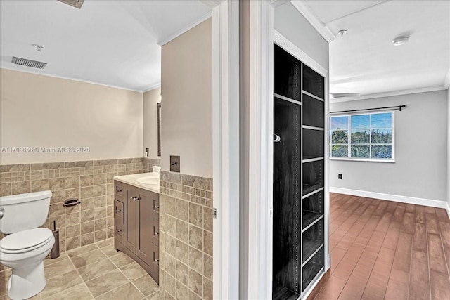 3659 NW Adriatic Ln Unit 305, Jensen Beach, FL 34957 - bathroom featuring crown molding, vanity, tile walls, toilet, and a wainscoted wall