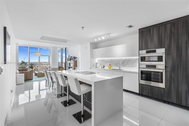 kitchen with white cabinets, sink, stainless steel double oven, a kitchen island, and dark brown cabinetry