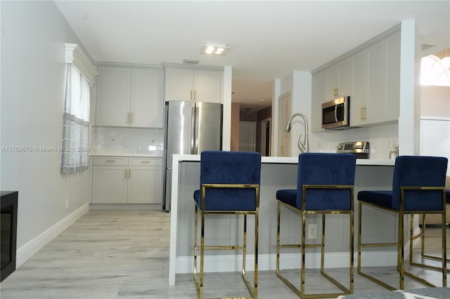 kitchen with stainless steel appliances, a kitchen bar, decorative backsplash, and light hardwood / wood-style flooring