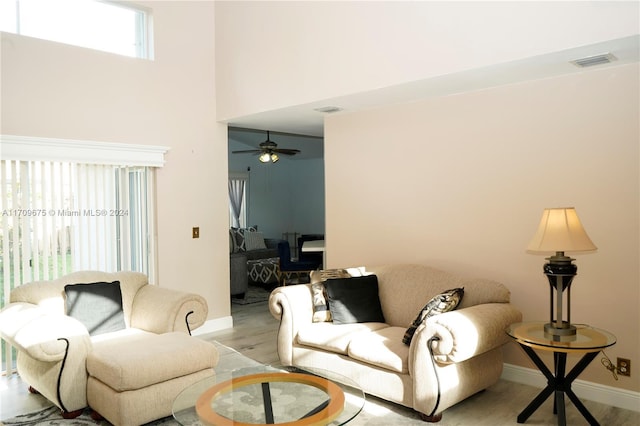 living room featuring ceiling fan, a high ceiling, and light wood-type flooring