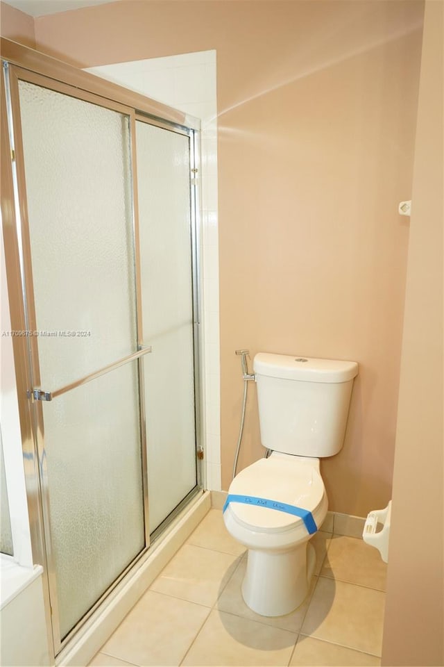 bathroom with a shower with door, tile patterned floors, and toilet