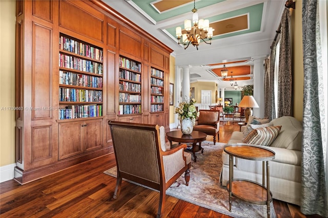 living area with decorative columns, ornamental molding, built in shelves, a notable chandelier, and dark hardwood / wood-style floors