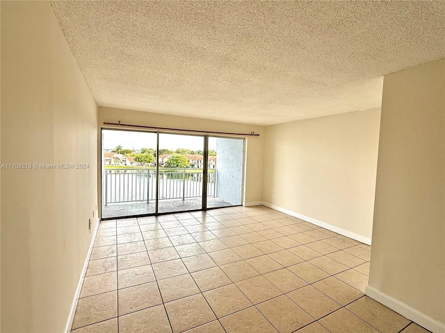 tiled empty room featuring a water view and a textured ceiling