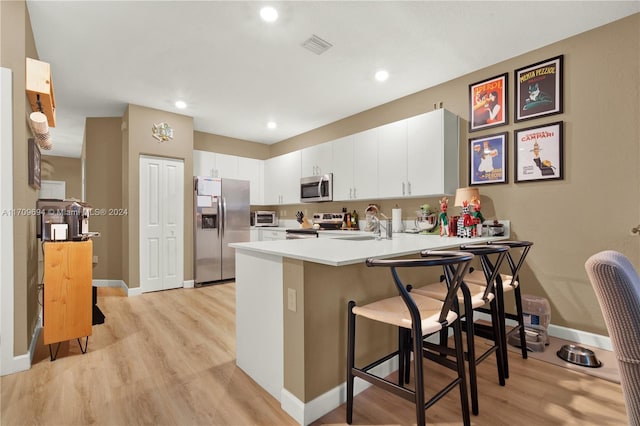 kitchen with kitchen peninsula, a breakfast bar, stainless steel appliances, and light hardwood / wood-style floors