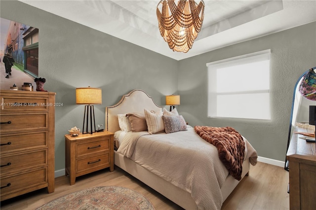 bedroom featuring a notable chandelier, light wood-type flooring, and a tray ceiling