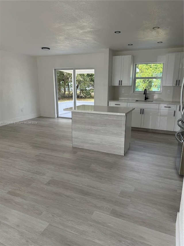 kitchen featuring a center island, sink, light wood-type flooring, tasteful backsplash, and white cabinetry