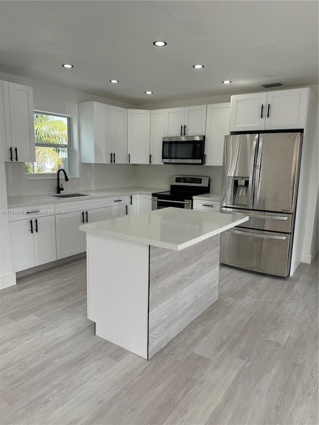 kitchen with appliances with stainless steel finishes, white cabinetry, a kitchen island, and sink