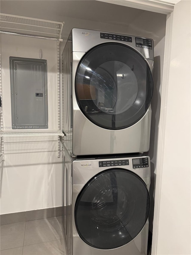 clothes washing area featuring tile patterned flooring, electric panel, and stacked washer / dryer