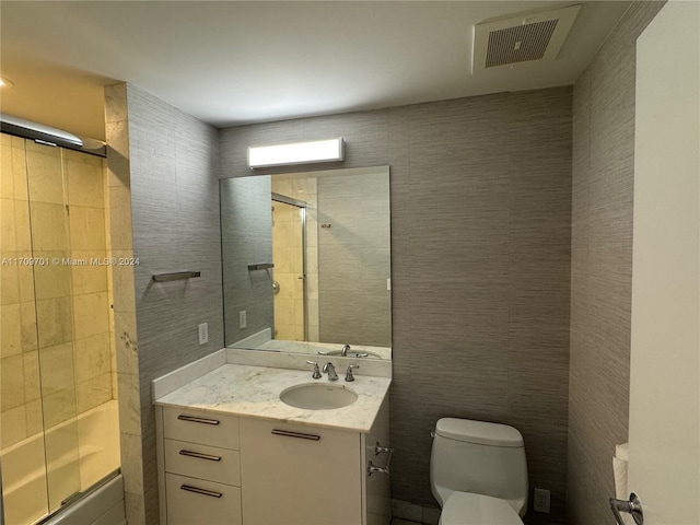 full bathroom featuring combined bath / shower with glass door, toilet, and tile walls