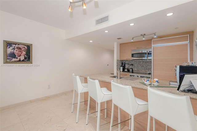 kitchen with decorative backsplash, light stone countertops, a breakfast bar, and sink