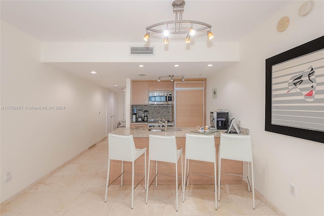 kitchen featuring backsplash, light stone counters, a breakfast bar, sink, and light brown cabinets