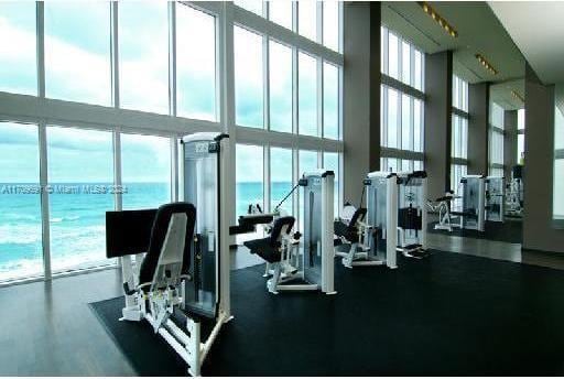 exercise room with expansive windows, a water view, a high ceiling, and a wealth of natural light