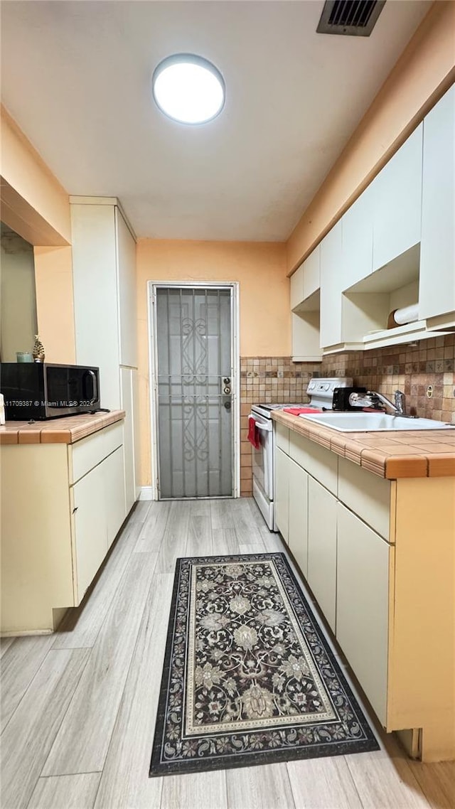 kitchen featuring tile counters, light wood-type flooring, white electric range, and sink