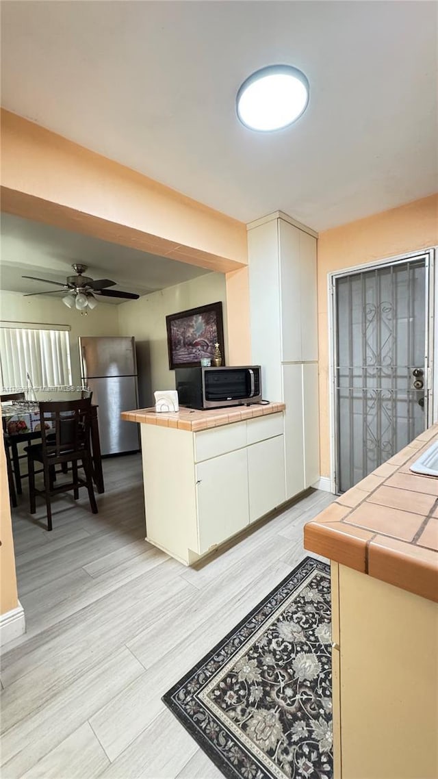 kitchen with ceiling fan, tile counters, light wood-type flooring, and appliances with stainless steel finishes